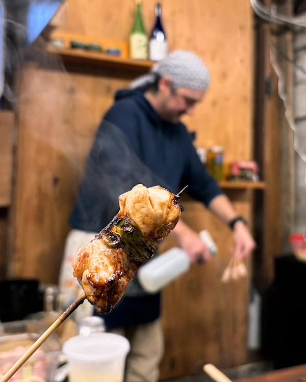 A steaming chicken thigh and onion skewer with a person cooking in the background