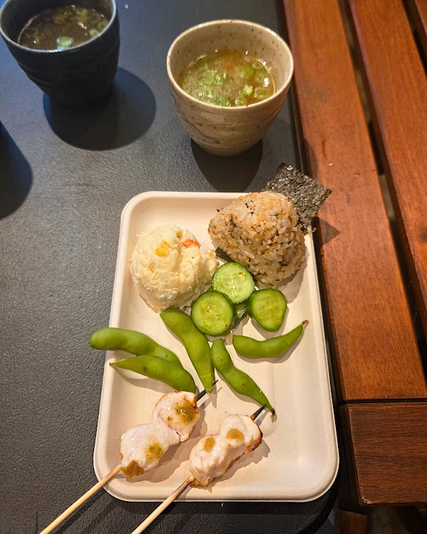 Breast and tender skewers along with onigiri, edamame, pickles and potato salad on a plate