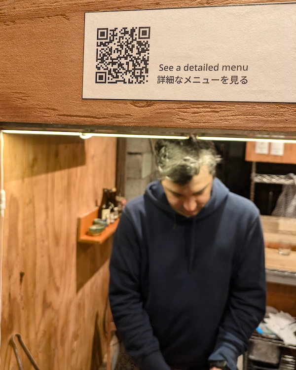 A man cooks on a grill while a sign directs guests to a detailed menu