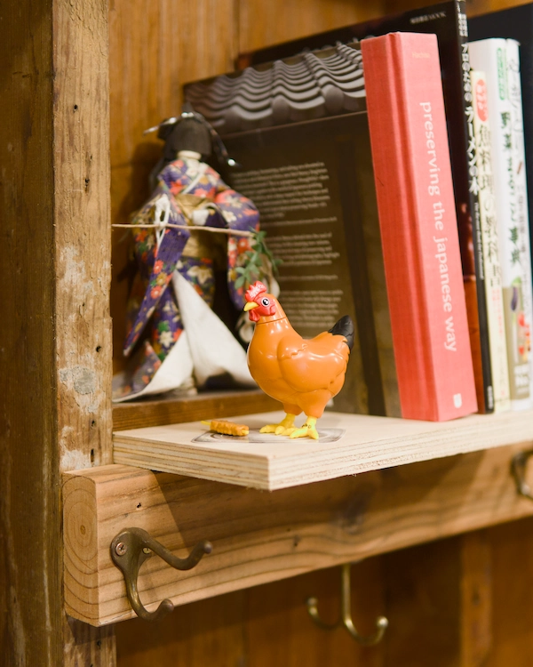 A small toy chicken sits on a shelf next to some books