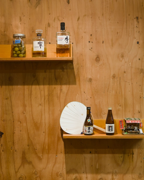 Bottles of Japanese whisky and sake site on shelves along a plywood wall